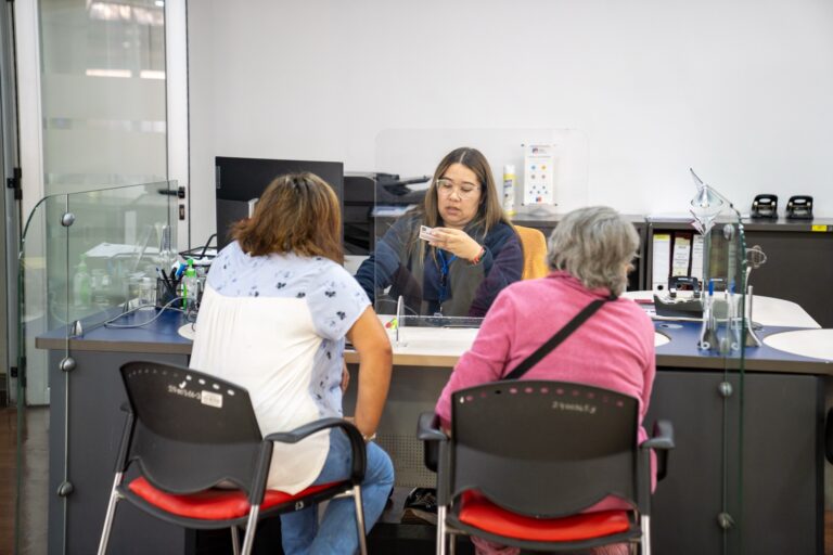 Funcionaria del IPS atendiendo a dos ciudadanas en módulo de atención con mampara de seguridad